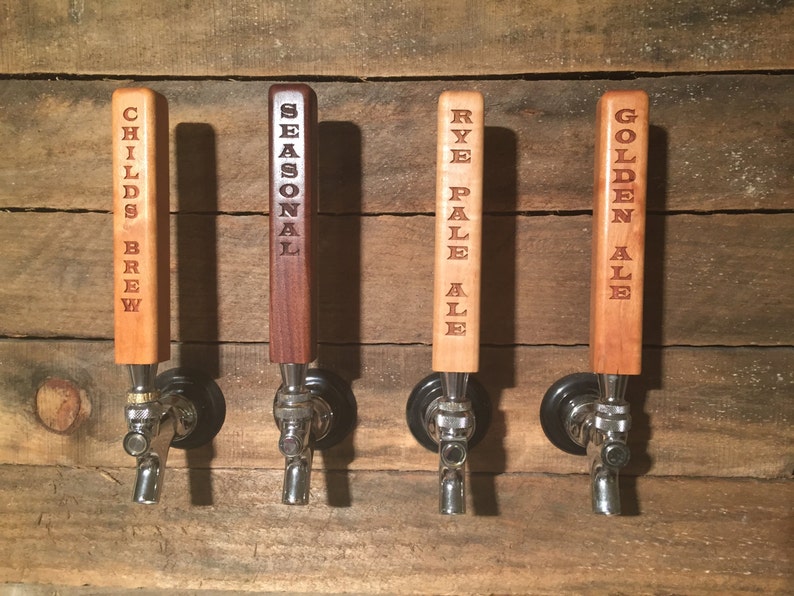 May include: Four wooden beer tap handles with different beer names engraved on them. The handles are mounted on a wooden wall. The names are "Childs Brew", "Seasonal", "Rye Pale Ale", and "Golden Ale".