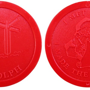 Könnte beinhalten: Roter Plastik-Token mit zwei Seiten. Eine Seite zeigt ein Cartoon-Bild von Rudolph, dem Rentier mit der roten Nase, das neben einem Wegweiser steht. Die andere Seite zeigt ein Cartoon-Bild vom Weihnachtsmann, der auf eine Liste schreibt mit dem Text "Ich habe den Weihnachtsmann getroffen Ich habe die nette Liste gemacht".