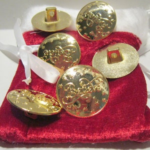 May include: Six gold-colored buttons with the word "Believe" embossed on them. The buttons are in a red velvet bag with a white ribbon.