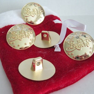 May include: Four gold-colored metal buttons with the word "Believe" engraved on them. The buttons are in a red velvet bag with a white drawstring.