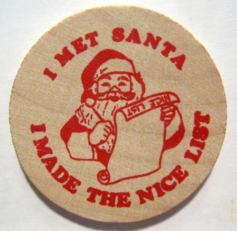 Puede incluir: Un token de papel redondo de color beige con texto rojo que dice "I Met Santa I Made The Nice List". Una imagen de dibujos animados de Santa Claus con un traje rojo y un sombrero sosteniendo un rollo que dice "Nice List".