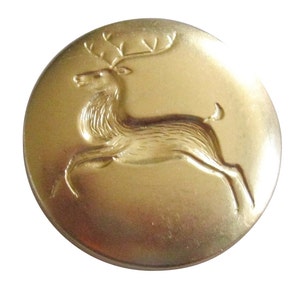 May include: A gold-colored metal button with a raised image of a deer with antlers. The deer is facing left and is in a running position.