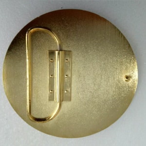 K&ouml;nnte beinhalten: Goldfarbener G&uuml;rtelverschluss aus Metall mit runder Form und einem Scharnierverschluss. Die Schnalle hat eine glatte, leicht strukturierte Oberfl&auml;che.