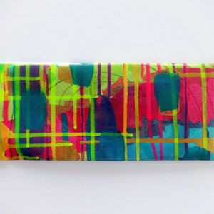 May include: A colorful clutch purse with a gold background and abstract design featuring bright pink, yellow, green, and blue paint splatters.