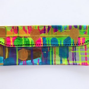 May include: A clear plastic clutch purse with a black stitched flap. The purse has a colorful abstract design with bright pink, green, blue, yellow, and gold accents.