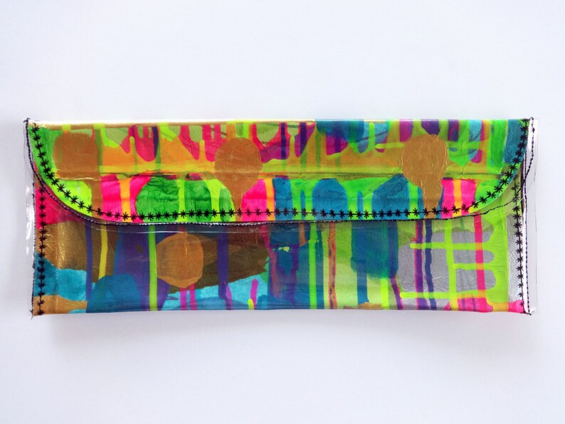 May include: A clear plastic clutch purse with a black stitched flap. The purse has a colorful abstract design with bright pink, green, blue, yellow, and gold accents.