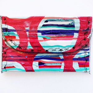 May include: A colorful clutch purse with a white background and red, blue, and green stripes. The purse has a black stitched border.
