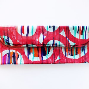 May include: A red, white, and blue clutch purse with a geometric pattern. The purse has a flap closure and a chain strap.