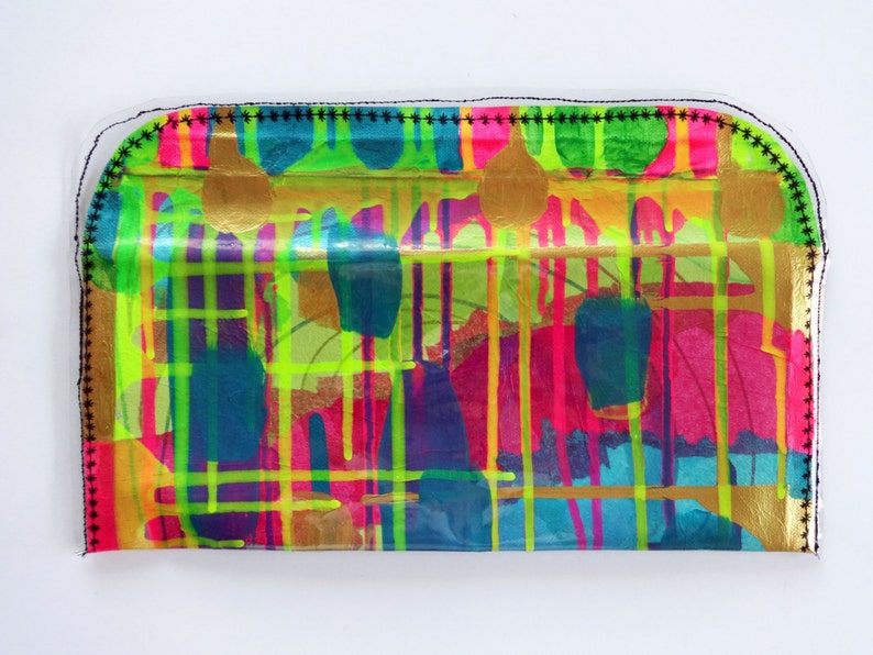 May include: A colorful clutch purse with a clear plastic front and a black stitched border. The front of the purse features a geometric pattern of bright colors, including yellow, green, pink, and blue, with gold accents.