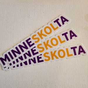 May include: Three white stickers with the word "MINNESKOLTA" printed in purple and yellow letters. The stickers are stacked on top of each other.
