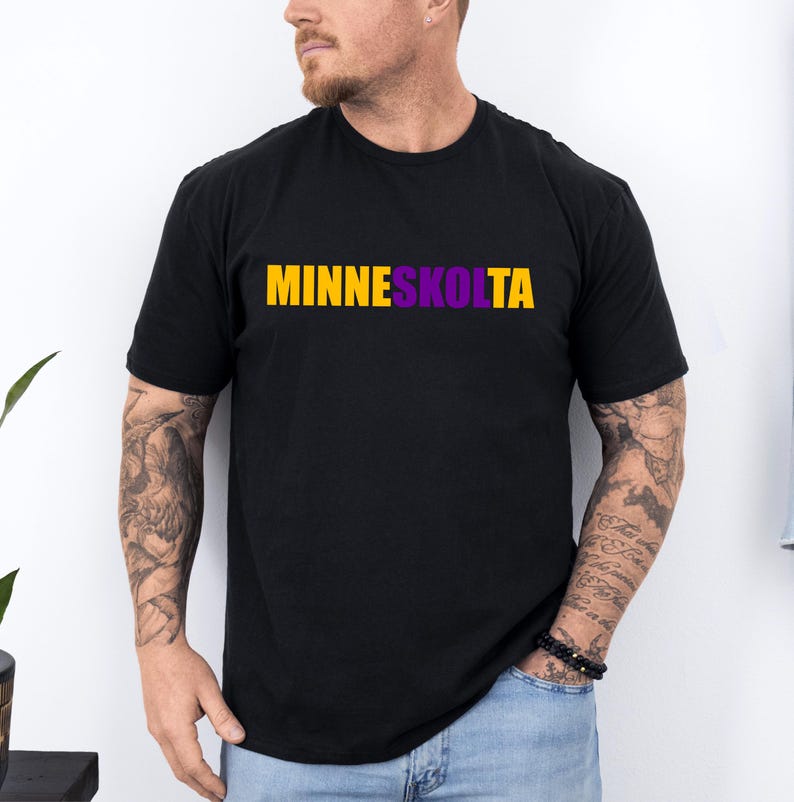 Op de afbeelding: Een zwart T-shirt met de tekst "MINNESKOLTA" in gele en paarse letters.