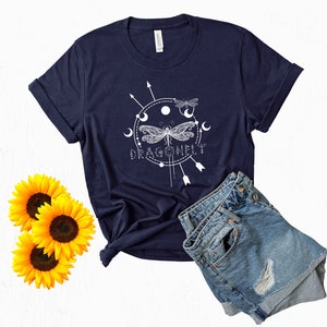 May include: A navy blue t-shirt with a white graphic of a dragonfly with a circle around it and the word "DRAGONFLY" underneath. The graphic also includes moons and arrows.