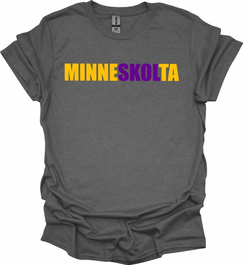 Op de afbeelding: Een donkergrijs T-shirt met de tekst "MINNESKOLTA" in gele en paarse letters.