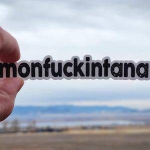 May include: A white sticker with black text that reads "monfuckintana".