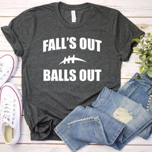 Puede incluir: Una camiseta gris oscuro con texto blanco que dice "Fall's Out Balls Out" y un gr&aacute;fico de f&uacute;tbol blanco.