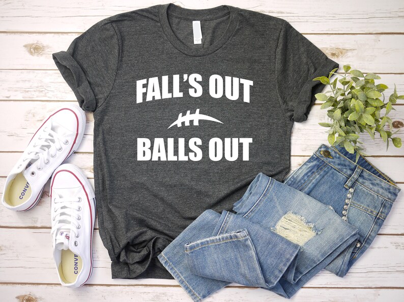 Puede incluir: Una camiseta gris oscuro con texto blanco que dice "Fall's Out Balls Out" y un gr&aacute;fico de f&uacute;tbol blanco.