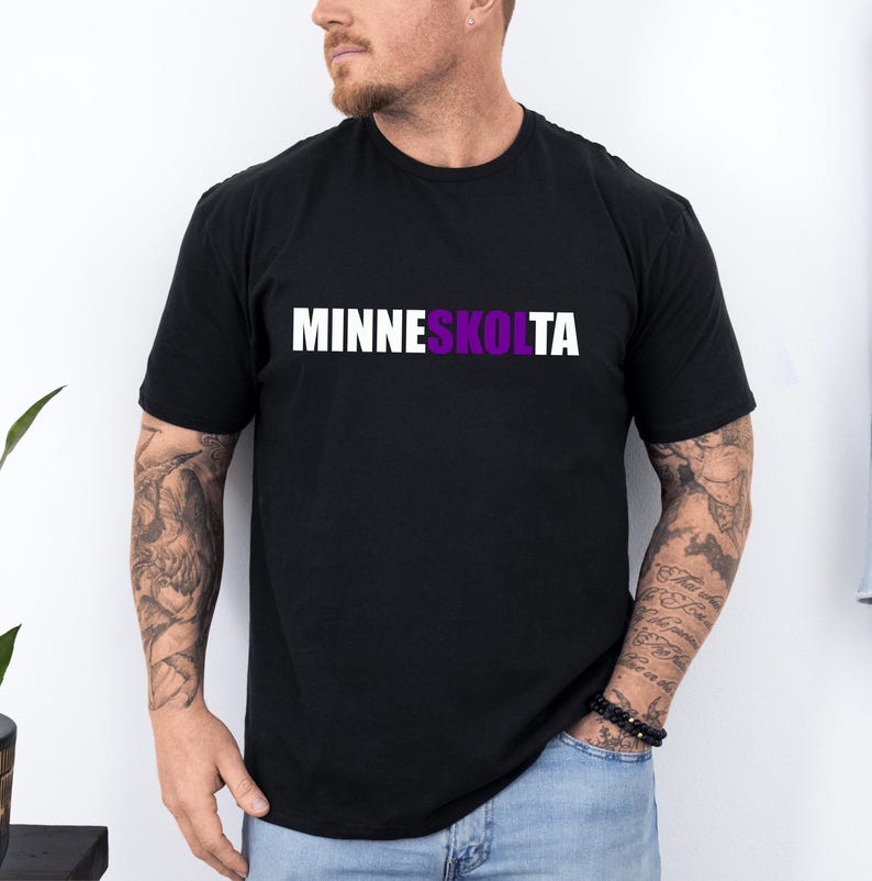 Op de afbeelding: Een zwart T-shirt met de tekst "MINNESKOLTA" in wit gedrukt, waarbij het gedeelte "KOLTA" in paars is.