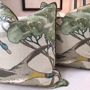 May include: Two green and brown throw pillows with a duck and tree pattern. The pillows have a green trim.