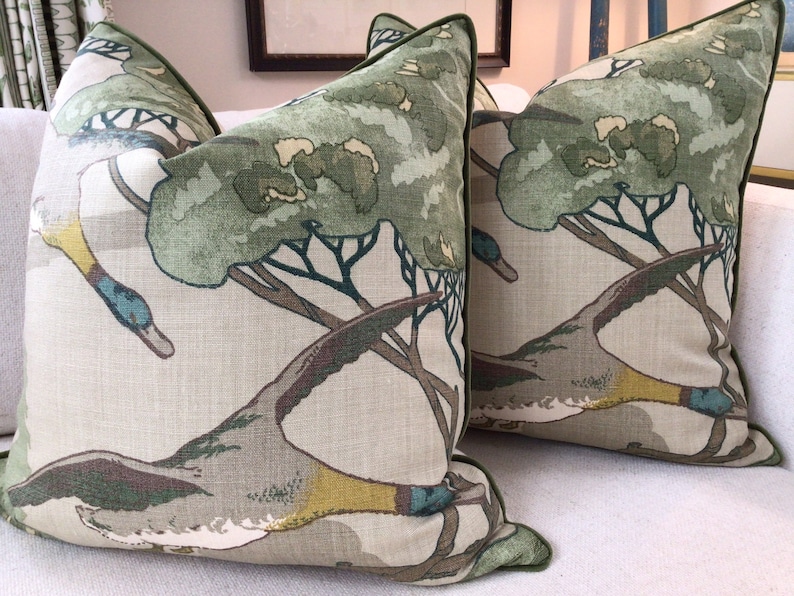 May include: Two green and brown throw pillows with a duck and tree pattern. The pillows have a green trim.