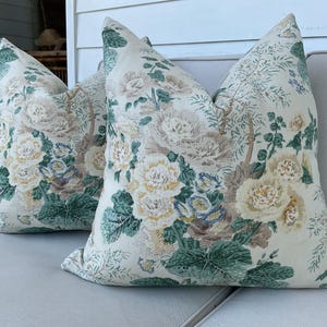 May include: Two decorative throw pillows with a floral pattern in shades of green, white, and brown. The pillows are on a white couch.