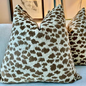 May include: Two brown and cream patterned throw pillows with a subtle leopard print design. The pillows are on a light blue couch.