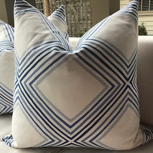 May include: Two white throw pillows with a blue and white geometric pattern. The pillows have a diamond shape with stripes running diagonally across the fabric.