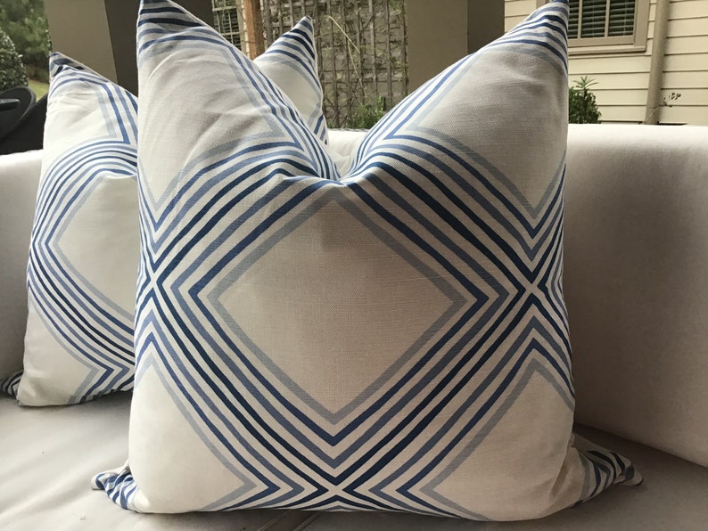 May include: Two white throw pillows with a blue and white geometric pattern. The pillows have a diamond shape with stripes running diagonally across the fabric.