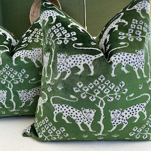 May include: Three green throw pillows with a white leopard print design. The pillows have a soft, velvety texture and a repeating pattern of leopards and stylized trees. The pillows are square and appear to be made of a plush fabric.