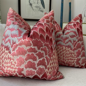 May include: Two red and cream throw pillows with a floral pattern. The pillows are on a white couch.