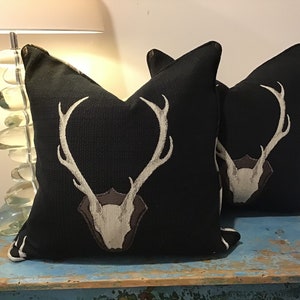 May include: Two black throw pillows with a white deer head design. The deer head is on a brown shield.