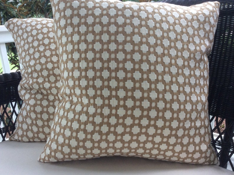 May include: Two brown and white patterned throw pillows with a geometric design. The pillows are on a white surface.