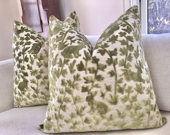 May include: Two green velvet cushion covers with a leafy pattern and a subtle embossed design. The cushions are on a white sofa.