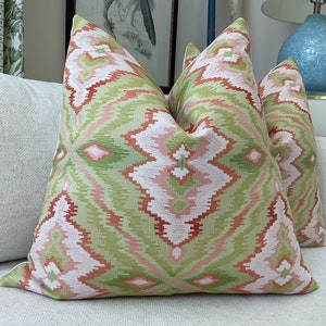 May include: Two decorative throw pillows with a pink, green, and red ikat pattern. The pillows are on a white couch.