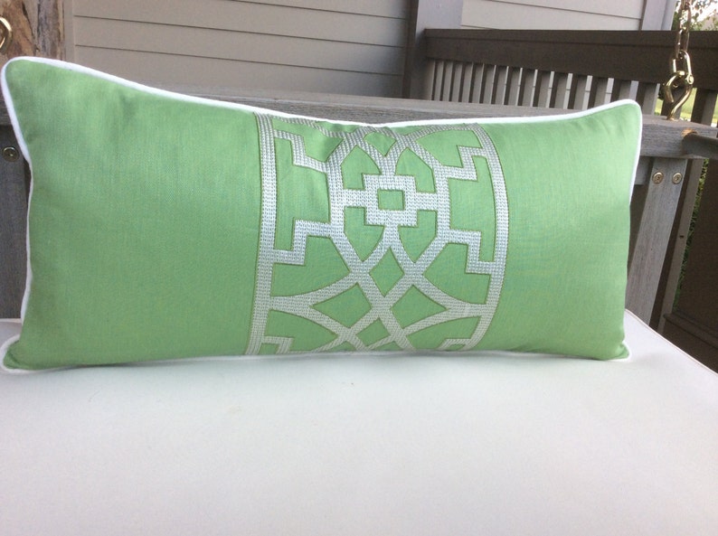 May include: A green lumbar pillow with a white geometric design. The pillow has a white piping around the edges.