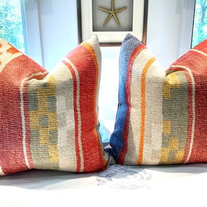 May include: Two decorative throw pillows with a striped pattern in shades of red, orange, yellow, blue, and gray. The pillows are made of a woven fabric and have a textured surface.