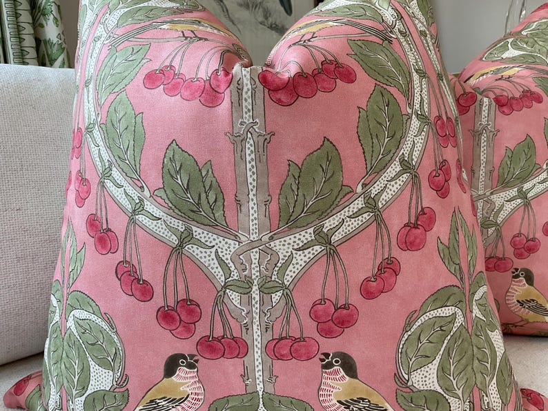May include: Pink pillow with a floral pattern featuring cherry blossoms and birds. The pillow has a white background with green leaves and pink cherries.