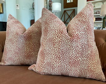 May include: Two throw pillows with a cream background and a red speckled pattern. The pillows are on a brown sofa.