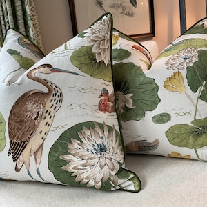 May include: Two decorative throw pillows with a green, white and brown floral pattern featuring water lilies, birds and leaves. The pillows have a green trim.