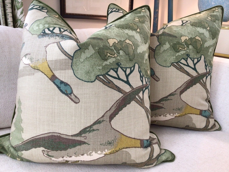 May include: Two green and brown throw pillows with a duck and tree design. The pillows have a green trim.