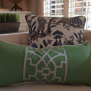 May include: Two decorative pillows on a white couch. The pillow in the foreground is green with a white geometric design. The pillow in the background is white with a floral pattern and blue and green accents.