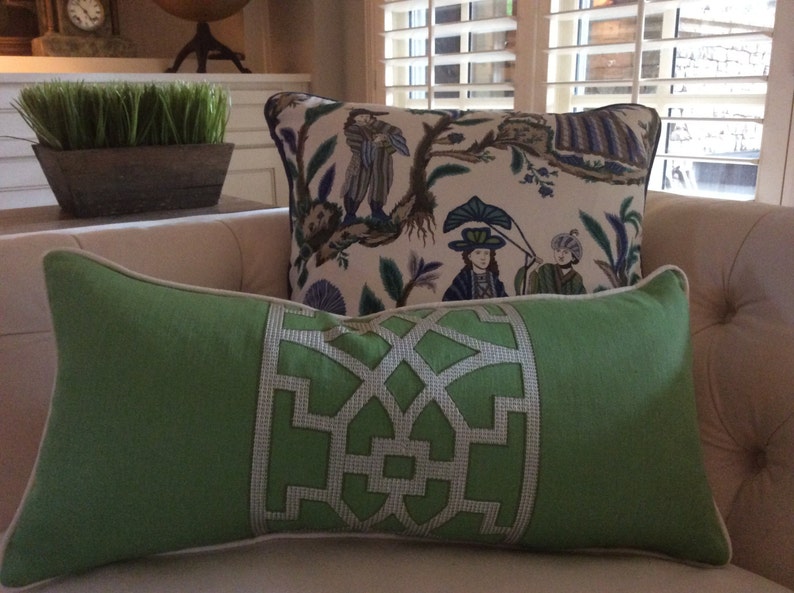 May include: Two decorative pillows on a white couch. The pillow in the foreground is green with a white geometric design. The pillow in the background is white with a floral pattern and blue and green accents.