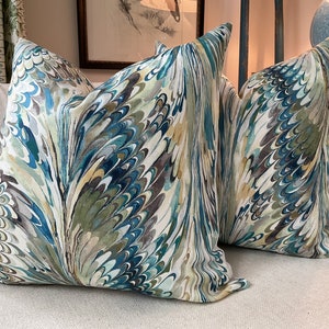 May include: Two decorative throw pillows with a blue, green, and brown marbled pattern. The pillows are on a white couch.