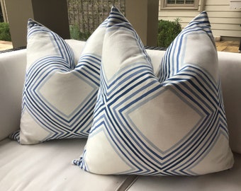 Puede incluir: Dos almohadas blancas con un patrón geométrico azul y blanco. El patrón presenta líneas diagonales y cuadrados.