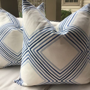 May include: Two white throw pillows with a blue and white geometric pattern. The pillows have a diamond shape with stripes running diagonally across the fabric.