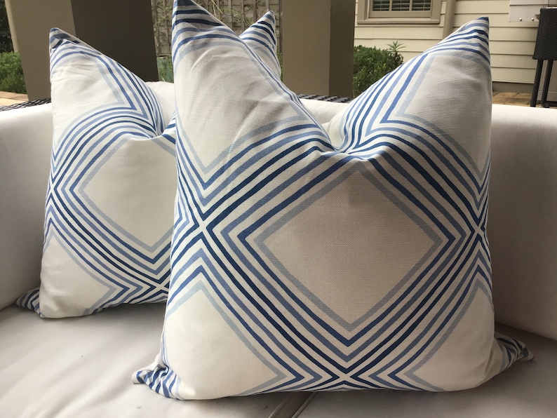 May include: Two white throw pillows with a blue and white geometric pattern. The pillows have a diamond shape with stripes running diagonally across the fabric.