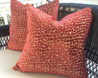 May include: Two red and gold patterned throw cushions with a textured, raised design. The cushions are on a black wicker chair.