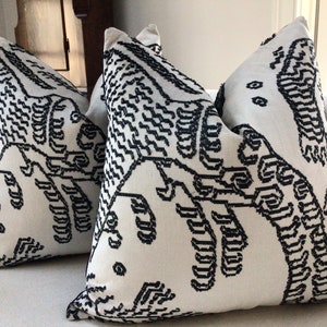 May include: Two white throw pillows with black geometric patterns. The patterns are abstract and resemble a stylized mountain range.