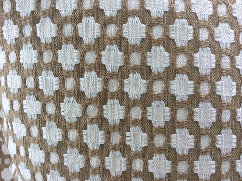May include: A close-up of a woven fabric with a geometric pattern. The fabric is brown and white, and the pattern is made up of small squares and circles.