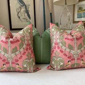 May include: Two pink and green throw pillows with a floral pattern and birds. The pillows have a repeating pattern of cherry blossoms and birds.