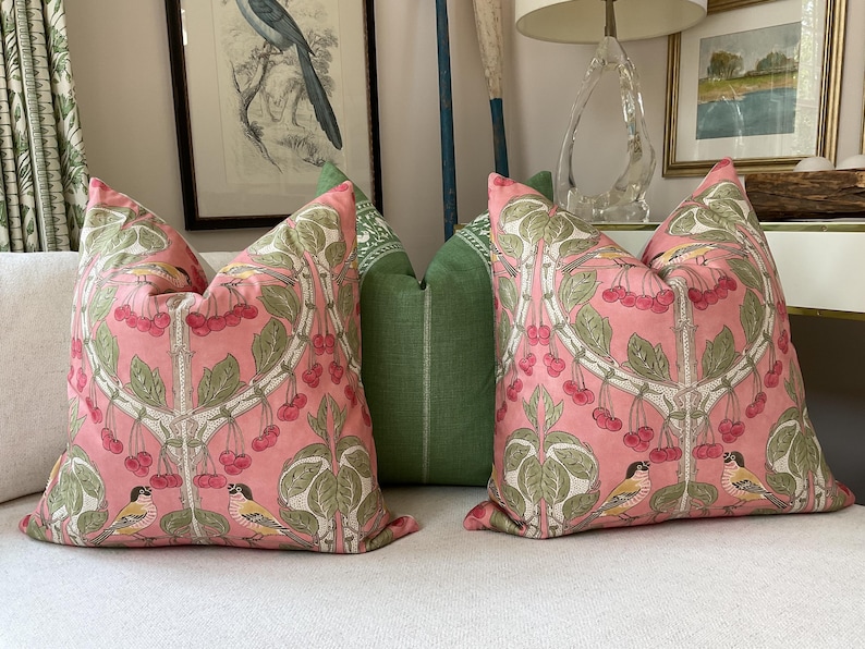 May include: Two pink and green throw pillows with a floral pattern and birds. The pillows have a repeating pattern of cherry blossoms and birds.